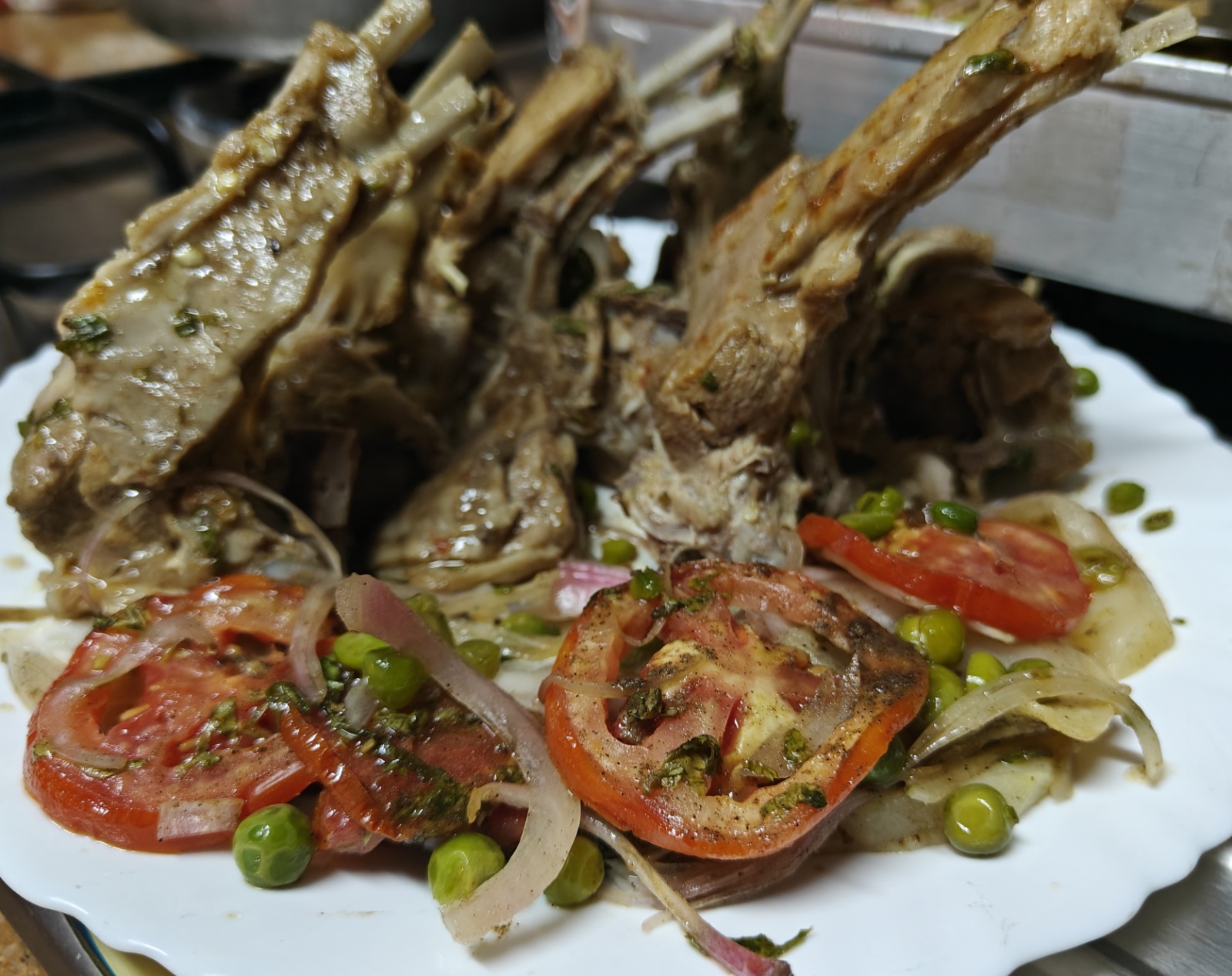 Rack of slow-cooked lamb chops plated with tomato and peas
