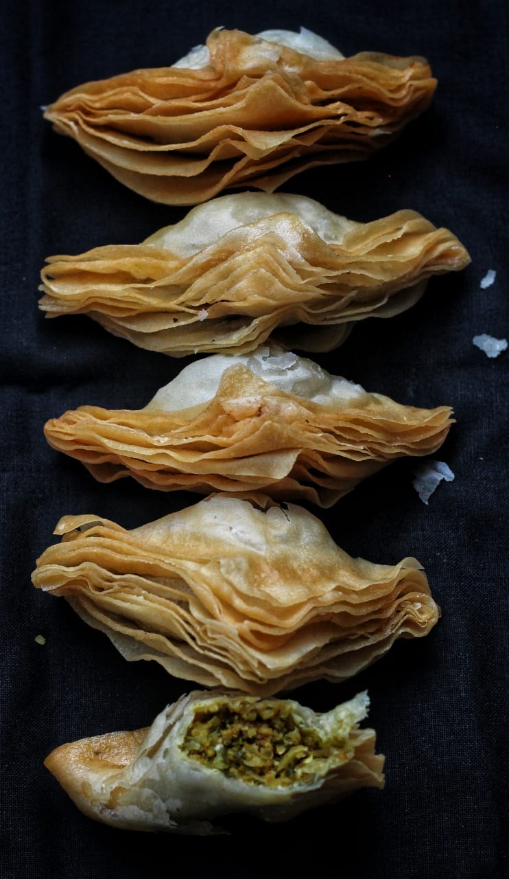 Layered warki samosas on a dark cloth