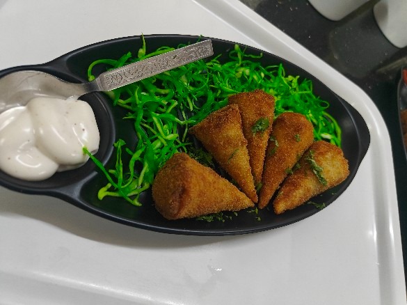 Golden smoky cone samosas with garlic dip on a black platter