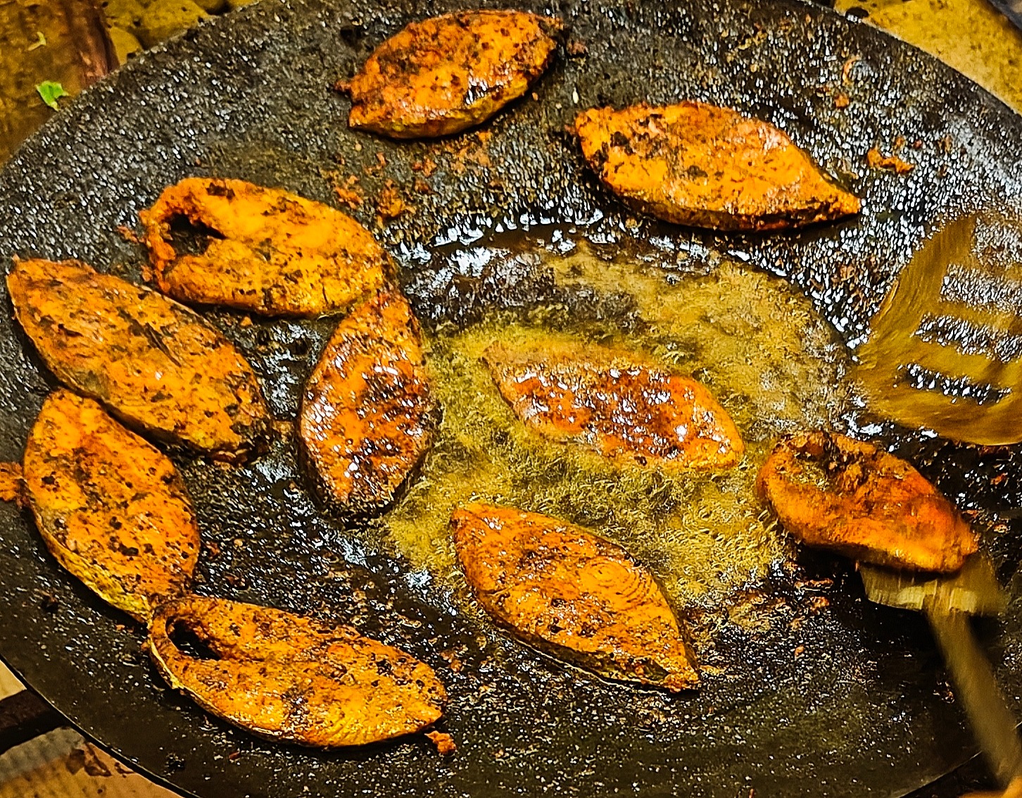 Masala coated fish slices frying on a hot tawa