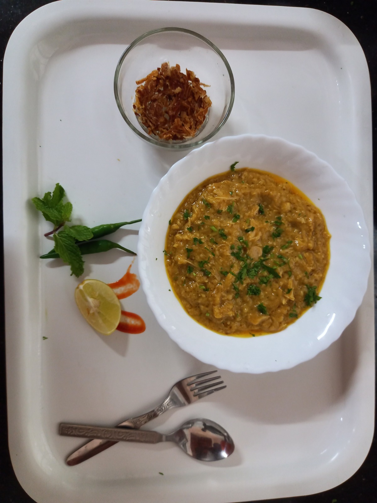 Bowl of haleem served with fried onions, lemon and green chilli